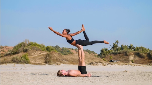 Fit sportliches Paar, das Acro Yoga mit Partner zusammen am Sandstrand praktiziert