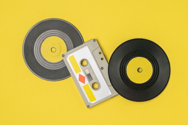 Fita cassete com fita magnética e discos de vinil em amarelo. Dispositivos retro para armazenar e reproduzir gravações de áudio.