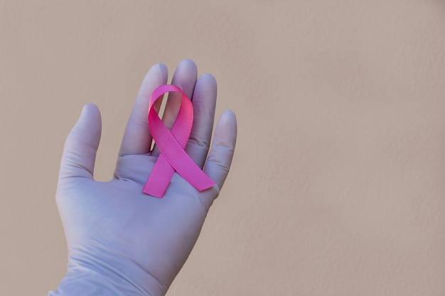 Fita com laço rosa na mão com luva cirúrgica. campanha de prevenção do câncer de mama. outubro rosa.