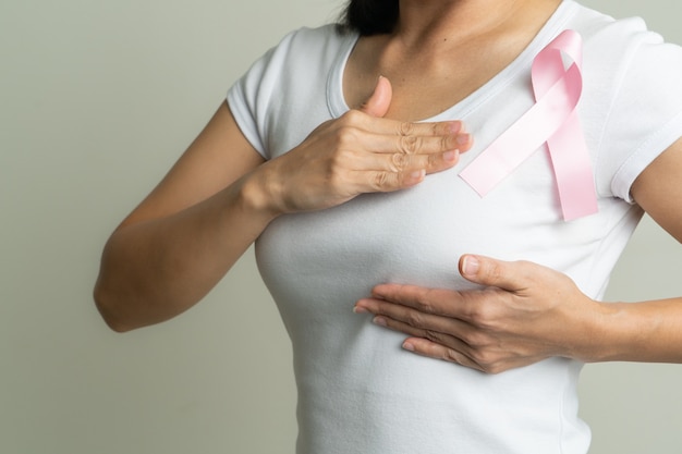 Fita crachá rosa no peito da mulher para apoiar a causa do câncer de mama. conceito de conscientização do câncer de mama