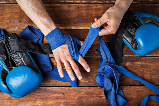 Fita de boxe de bandagem de homem em suas mãos antes da luta de boxe em uma superfície de madeira. O conceito de treinamento para boxe, treinamento ou luta. Vista plana, vista superior