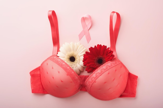 Fita de conscientização do câncer de mama Gerberas de sutiã branco e vermelho com fita de fita rosa deitada no sutiã feminino em fundos Conscientização do câncer de mama e outubro Dia rosa dia mundial do câncer Vista superior Mock up