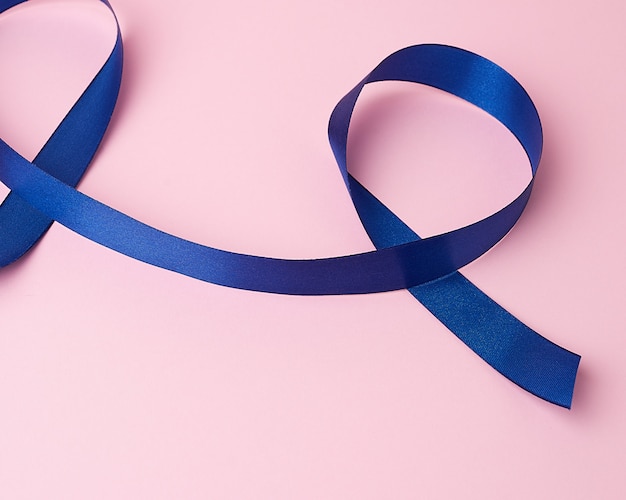 Foto fita de seda azul escura torcida em loops em um fundo rosa