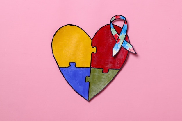 Fita do Dia Mundial da Conscientização do Autismo em forma de coração de quebra-cabeça colorida isolada em fundo rosa