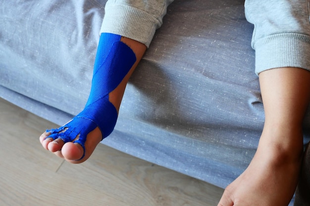 Foto fita elástica terapêutica azul aplicada à terapia de cinesioterapia na perna de uma criança para lesões