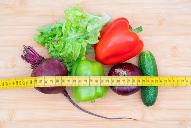Fita métrica amarela e legumes em uma tábua de madeira. Dieta de estilo de vida saudável.