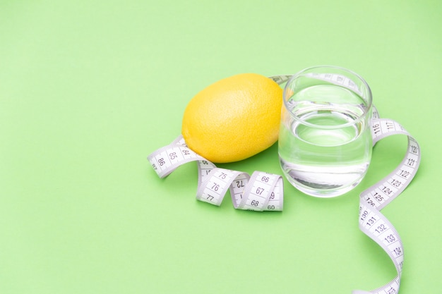 Fita métrica com copo de água e limão sobre fundo verde. Conceito de dieta. Espaço de cópia gratuita.