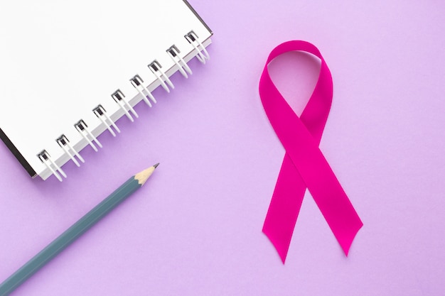 Fita rosa e bloco de notas em uma mesa roxa, o conceito de saúde feminina, a luta contra o câncer de mama