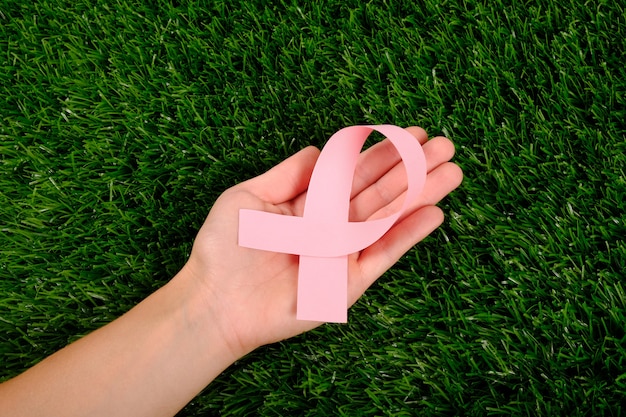 Foto fita rosa na mão na palma da mão na grama verde. símbolo de luta contra o câncer.