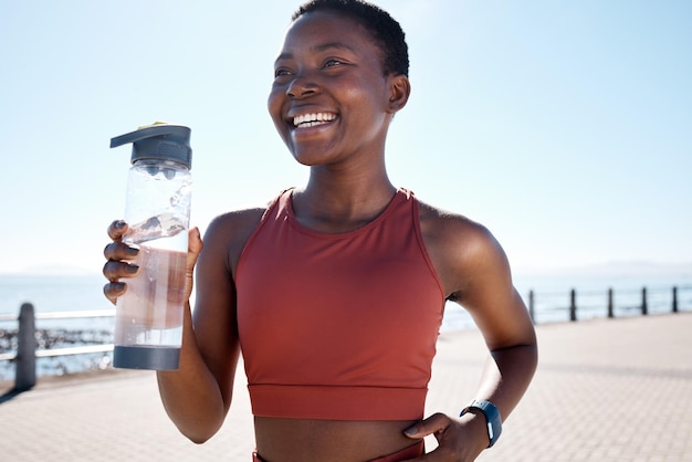 Fitness de agua potable y mujer negra corriendo junto al mar para entrenamiento deportivo y ejercicio Relajarse libertad y sonrisa deportiva de un atleta corredor feliz por la energía cardiovascular y el bienestar de la salud