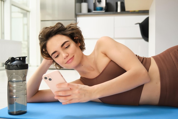 Fitness y bienestar en línea retrato de una mujer joven acostada en una alfombra de yoga mirando la aplicación de teléfono inteligente loo
