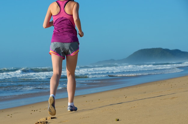 Fitness y correr en la playa, piernas de mujer corredor en zapatos en la arena cerca del mar, estilo de vida saludable y concepto deportivo