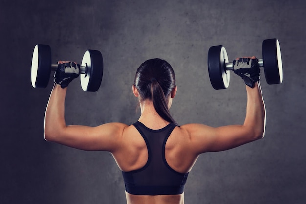 fitness, deporte, ejercicio, entrenamiento y concepto de personas - mujer joven flexionando músculos con pesas en el gimnasio