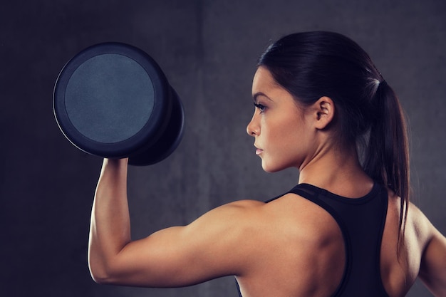 fitness, deporte, ejercicio, entrenamiento y concepto de personas - mujer joven flexionando músculos con pesas en el gimnasio