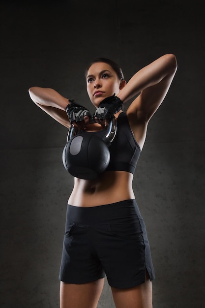 fitness, deporte, ejercicio, levantamiento de pesas y concepto de personas - mujer joven flexionando músculos con pesas rusas en el gimnasio