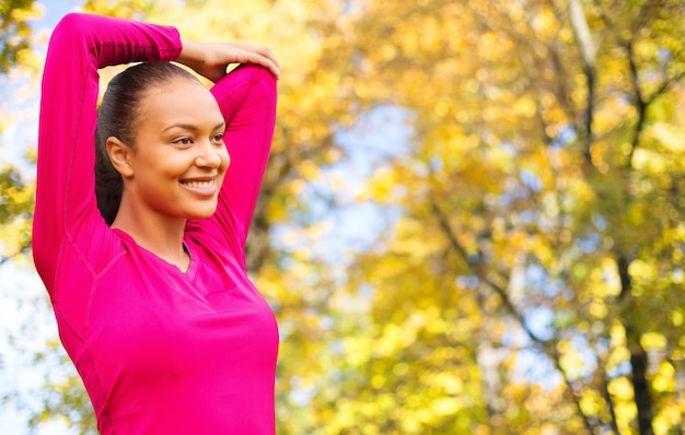 fitness, deporte, entrenamiento y concepto de personas - mujer sonriente estirando la mano sobre el fondo del parque de otoño