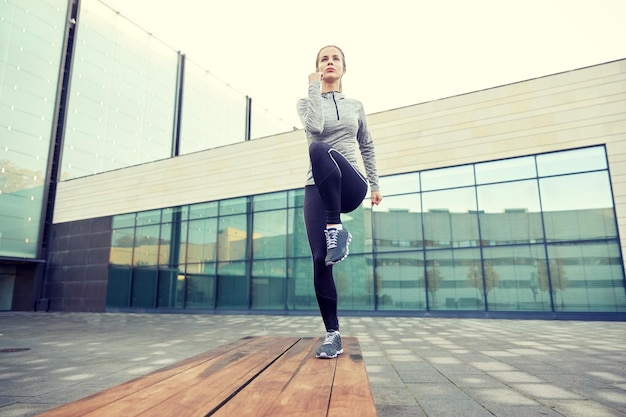 fitness, deporte, entrenamiento, personas y concepto de estilo de vida - mujer joven haciendo ejercicio de paso en el banco de la calle de la ciudad