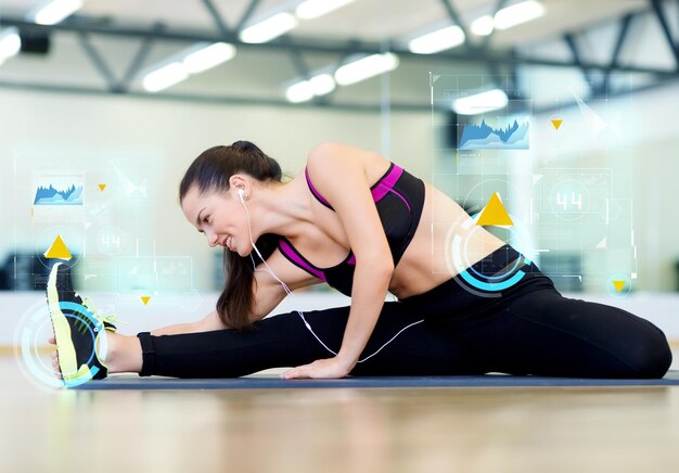 fitness, deporte, entrenamiento, tecnología y concepto de estilo de vida - mujer joven sonriente que se estira en la alfombra en el gimnasio