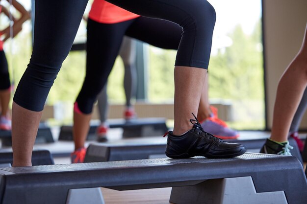 fitness, deporte, gente, aeróbicos escalonados y concepto de estilo de vida - cierre de piernas de mujeres haciendo ejercicio con escaladores en el gimnasio