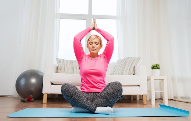 fitness, deporte, gente y concepto de estilo de vida saludable - mujer feliz de talla grande estirando la pierna en la alfombra en casa