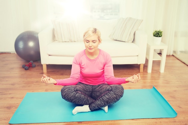 fitness, deporte, gente y concepto de estilo de vida saludable - mujer feliz de talla grande estirando la pierna en la alfombra en casa