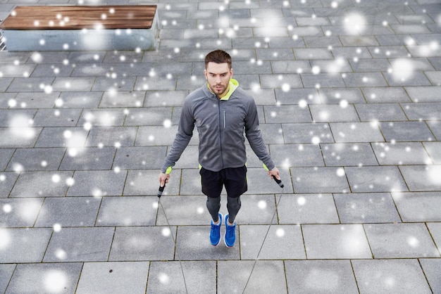 fitness, deporte, gente, ejercicio y estilo de vida saludable concepto - hombre saltando con cuerda de salto al aire libre sobre la nieve