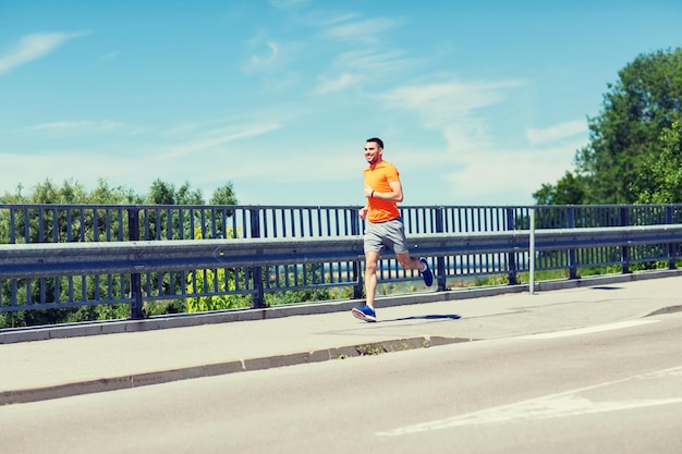 fitness, deporte, gente, tecnología y concepto de estilo de vida saludable - joven sonriente con reloj de frecuencia cardíaca corriendo en la playa de verano