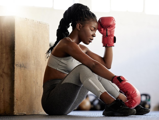 Fitness deportivo y boxeadora en descanso del ejercicio y entrenamiento en el piso de un gimnasio Atleta negra que parece exhausta con poca energía durante un entrenamiento de rutina Mujer descansando después de un partido físico