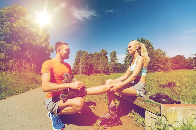 fitness, desporto, verão, casal e conceito de estilo de vida saudável - homem feliz a ajudar a mulher a andar de patins ao ar livre