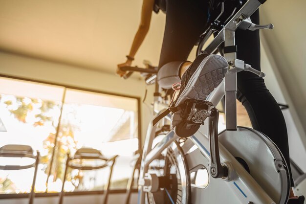 Fitness, entrenamiento, ejercicio de gimnasio, estilo de vida y concepto saludable. Vista trasera del entrenamiento de la mujer con bicicleta. Las mujeres hacen ejercicio en el gimnasio para un estilo de vida saludable en bicicleta al atardecer.