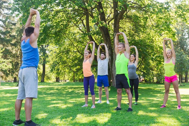 fitness, esporte, amizade e conceito de estilo de vida saudável - grupo de amigos adolescentes felizes ou desportistas exercitando e esticando as mãos no campo de treinamento