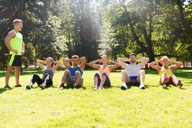 fitness, esporte, amizade e conceito de estilo de vida saudável - grupo de amigos adolescentes felizes ou desportistas exercitando e fazendo abdominais no campo de treinamento