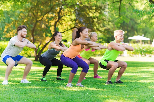 fitness, esporte, amizade e conceito de estilo de vida saudável - grupo de amigos adolescentes felizes ou desportistas exercitando e fazendo agachamentos no acampamento