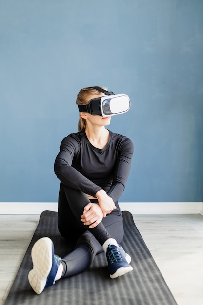 Fitness, esporte e tecnologia. jovem mulher atlética usando óculos de realidade virtual, sentada no tapete de ginástica