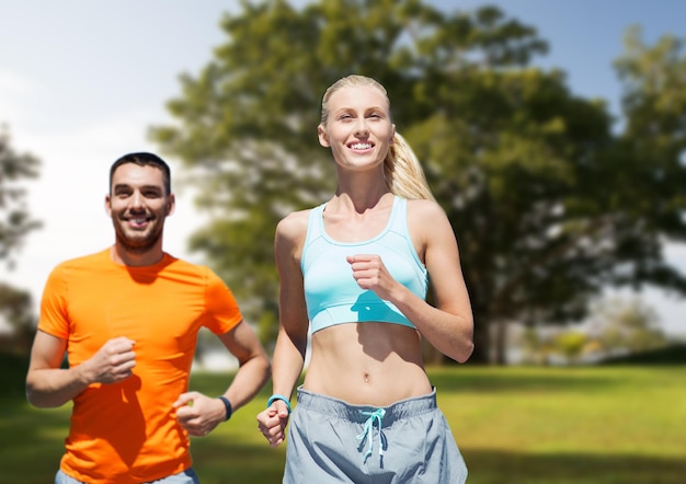 fitness, esporte, exercício e conceito de estilo de vida saudável - casal sorridente correndo ou correndo sobre o fundo do parque de verão