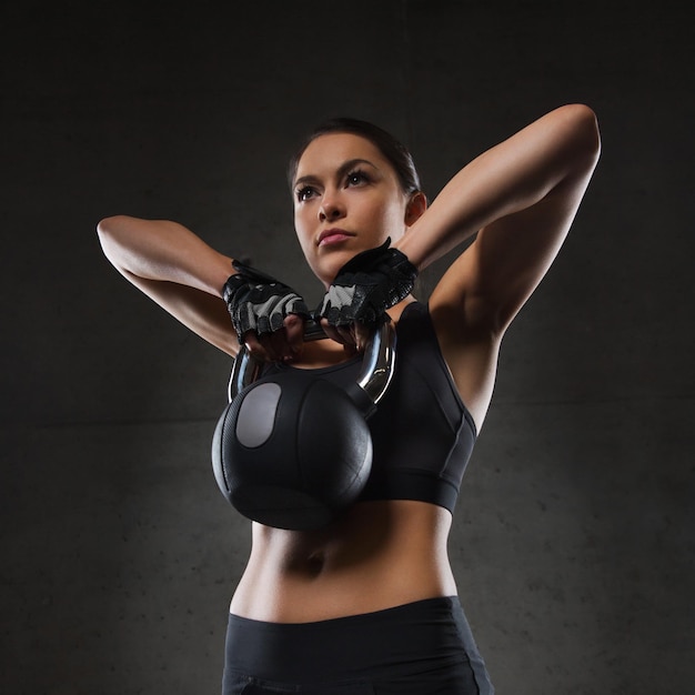 fitness, esporte, exercício, levantamento de peso e conceito de pessoas - jovem flexionando os músculos com kettlebell no ginásio