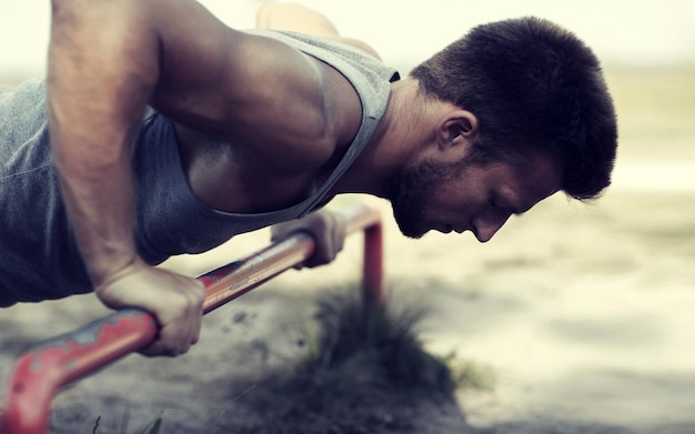 Foto fitness, esporte, exercício, treinamento e conceito de estilo de vida - jovem fazendo flexões na barra horizontal ao ar livre