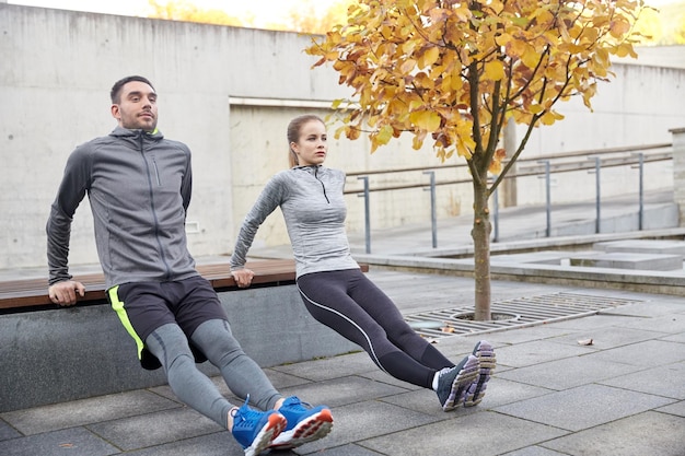 fitness, esporte, exercício, treinamento e conceito de pessoas - casal fazendo exercício de mergulho de tríceps no banco da rua da cidade