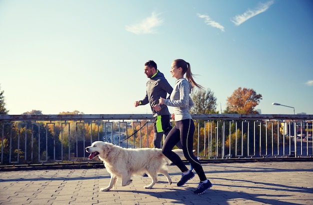 fitness, esporte, pessoas e conceito de corrida - casal feliz com cachorro correndo ao ar livre