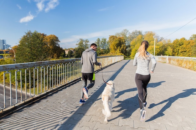 fitness, esporte, pessoas e conceito de corrida - close-up de casal com cachorro correndo ao ar livre