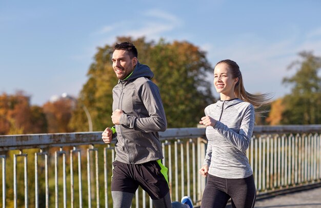 fitness, esporte, pessoas e conceito de estilo de vida - casal feliz correndo ao ar livre