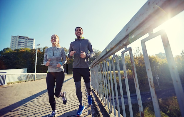 fitness, esporte, pessoas e conceito de estilo de vida - casal feliz correndo ao ar livre