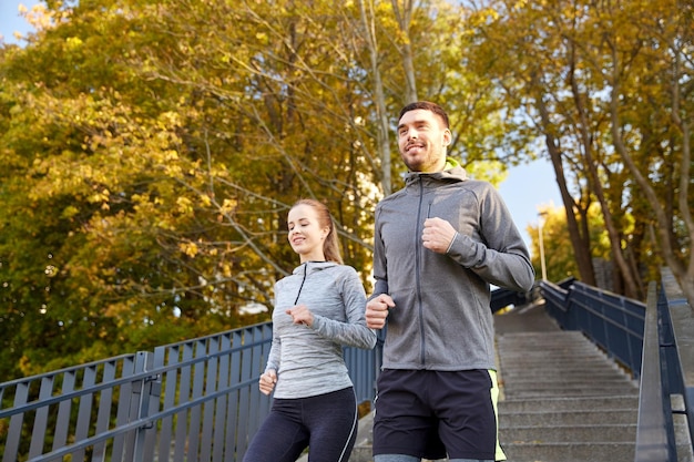 fitness, esporte, pessoas e conceito de estilo de vida - casal feliz correndo lá embaixo na cidade