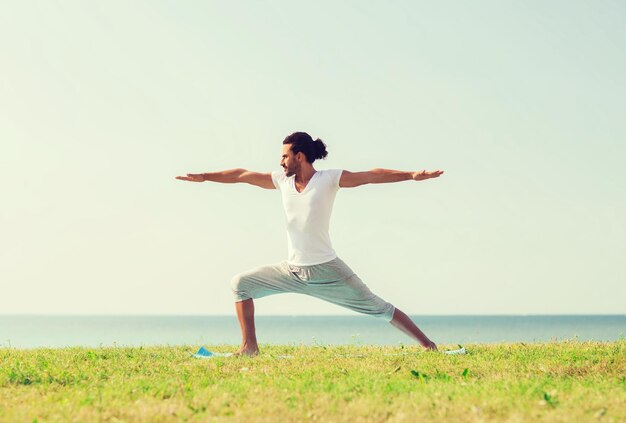 fitness, esporte, pessoas e conceito de estilo de vida - homem sorridente fazendo exercícios de ioga ao ar livre