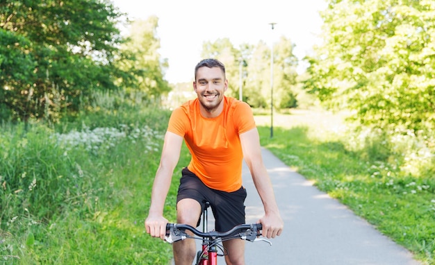 fitness, esporte, pessoas e conceito de estilo de vida saudável - jovem feliz andando de bicicleta ao ar livre