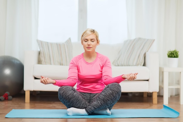 fitness, esporte, pessoas e conceito de estilo de vida saudável - mulher de tamanho grande feliz esticando a perna no tapete em casa