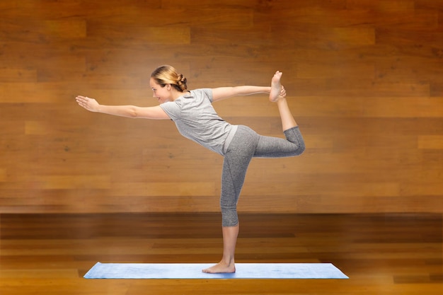 fitness, esporte, pessoas e conceito de estilo de vida saudável - mulher fazendo ioga no senhor da pose de dança na esteira sobre o fundo do quarto de madeira