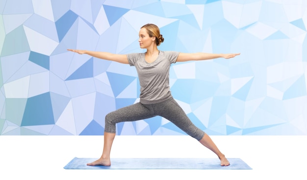 fitness, esporte, pessoas e conceito de estilo de vida saudável - mulher fazendo pose de guerreiro de ioga na esteira sobre fundo azul poligonal