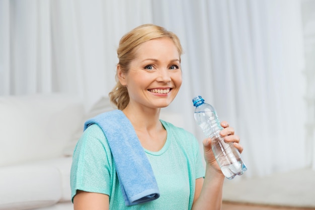 fitness, esporte, pessoas e conceito de estilo de vida saudável - mulher feliz com garrafa de água bebendo depois de se exercitar em casa