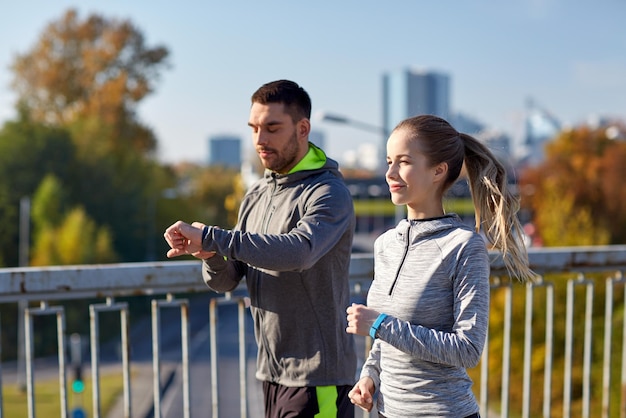 fitness, esporte, pessoas, tecnologia e conceito de estilo de vida saudável - casal sorridente com relógio de frequência cardíaca correndo sobre a ponte da rodovia da cidade